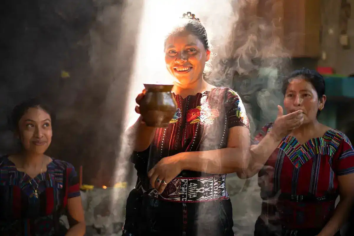 Woman holding ceremonial cacao in traditional Mayan attire, surrounded by smoke and cultural ritual