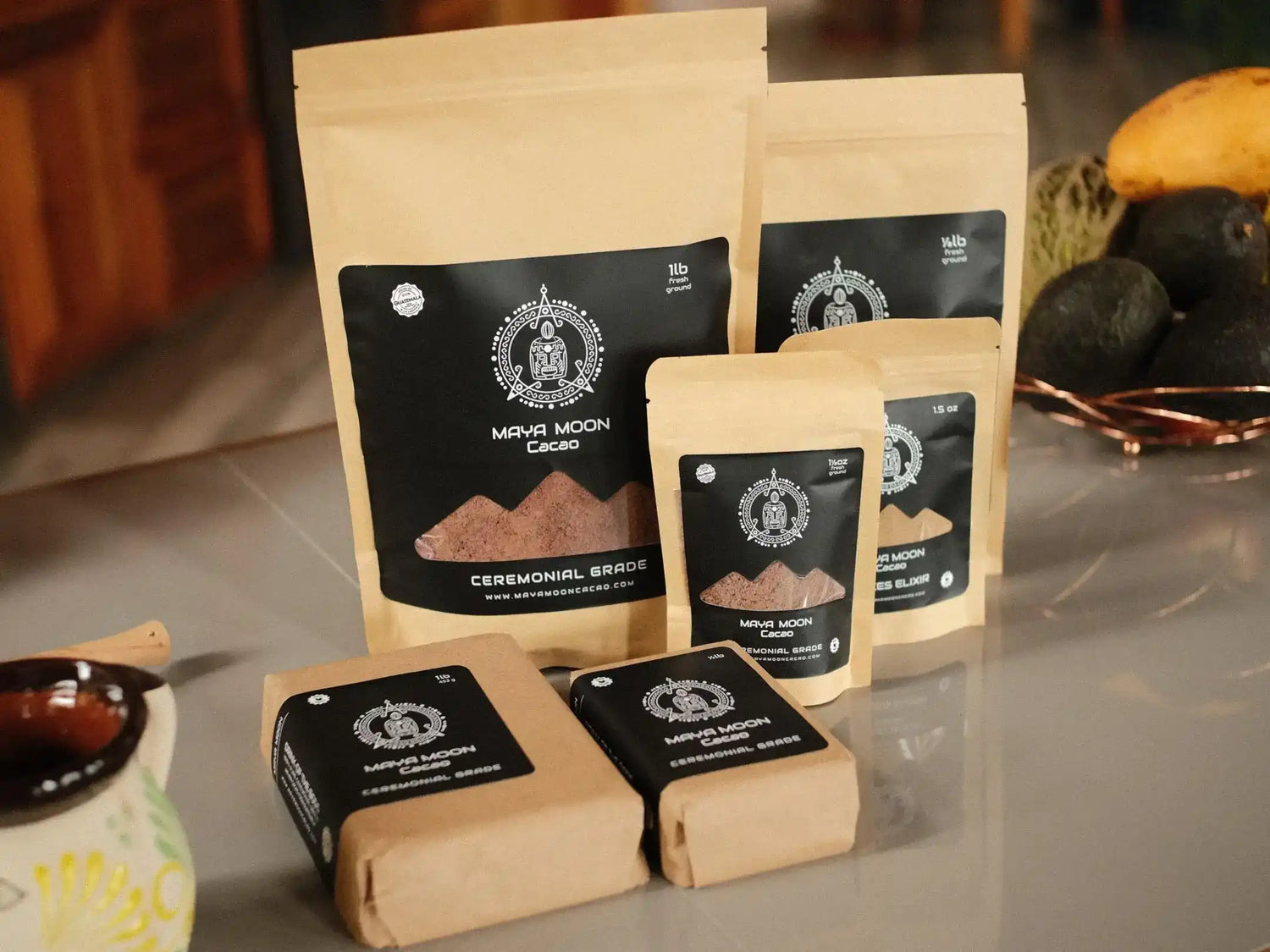 Several pouches and wrapped blocks of Maya Moon wholesale Ceremonial Raw Cacao powder products arranged on a countertop in a kitchen setting.