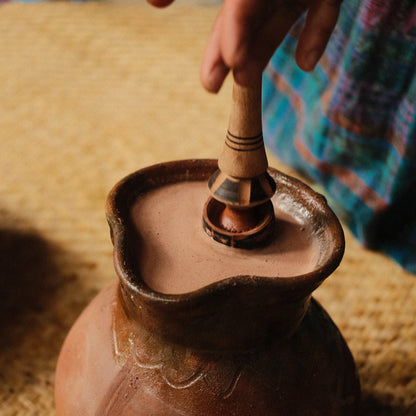 Hand holding cacao nibs above traditional molinillo whisk, molinillo de chocolate, cocoa mixer, ceremonila cacao tool 